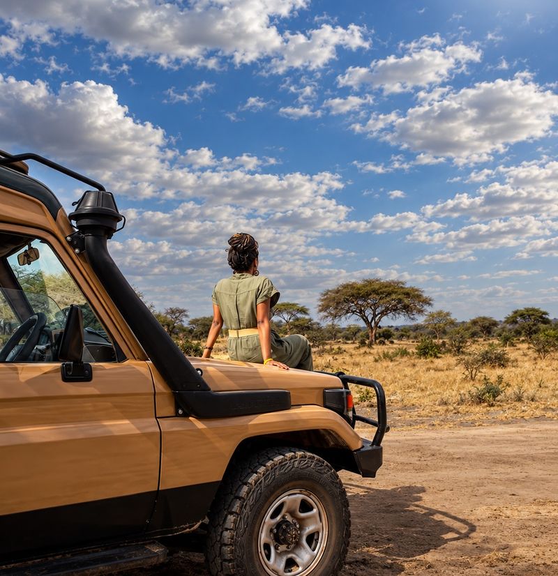Traveller resting on a safari vehicle under a wide blue sky